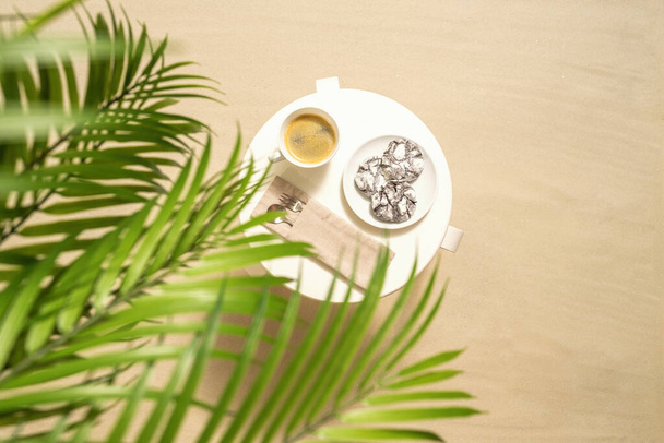 Cup of coffee with chocolate cookies on the table under palm trees on the sandy beach. Outdoors cafe. Top view - Foto, imagen