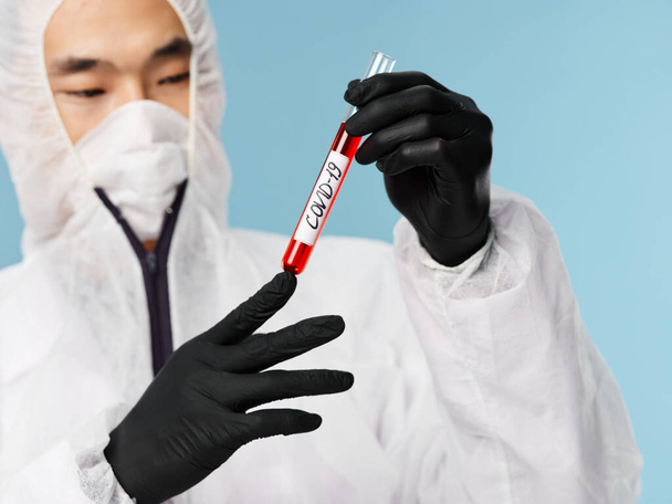 Hombre asiático ropa protectora guantes negros examen de sangre fondo azul - Foto, imagen
