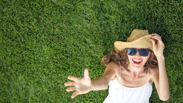 Womna wearing hat and sunglasses and lying on green grass, top view  - Foto, Imagem