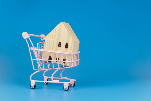 Panier avec maison en bois sur fond bleu, concept de vente et d'achat d'entreprise. - Photo, image
