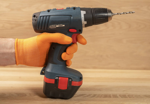 Male hand in building gloves holding professional cordless drill tool or machine for using in repair and construction. - Valokuva, kuva