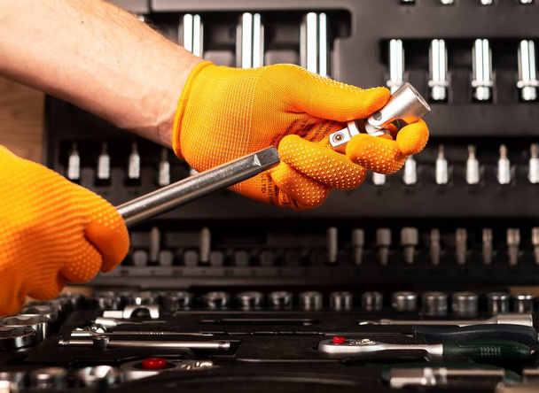 Male hand in glove holding metal handle extension tool, taking it from toolbox. - Photo, Image