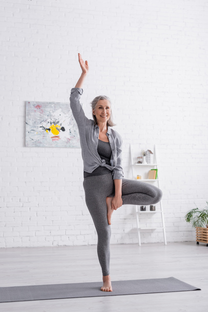 happy middle aged woman in sportwear practicing yoga on mat at home  - Fotografie, Obrázek