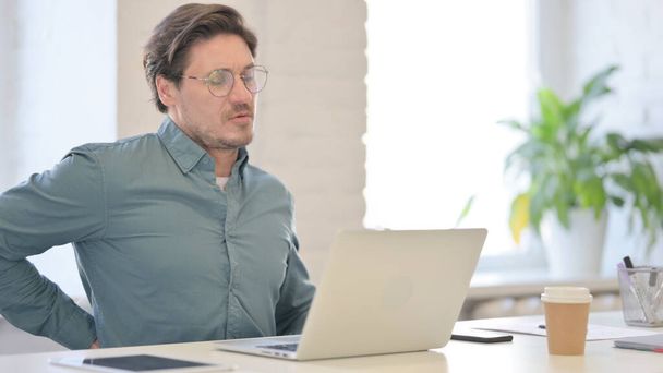 Uomo di mezza età con computer portatile con mal di schiena - Foto, immagini