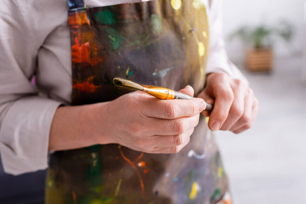 Üzerinde boya fırçası olan önlüklü orta yaşlı bir sanatçının kısmi görüntüsü  - Fotoğraf, Görsel
