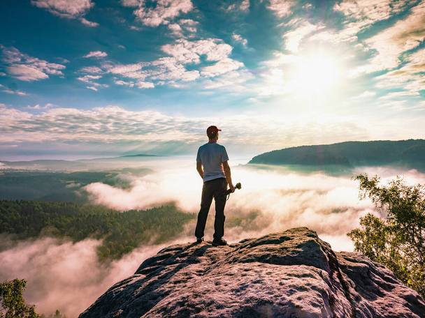 Artiste avec caméra et trépied regarder lever de soleil sur le sommet rocheux. Le photographe profite du lever du soleil d'automne brumeux sur une falaise abrupte dans le parc national de la Suisse saxonne. - Photo, image