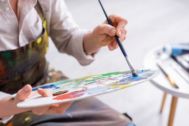 cropped view of middle aged woman holding paintbrush and palette with colorful paints  - Фото, изображение