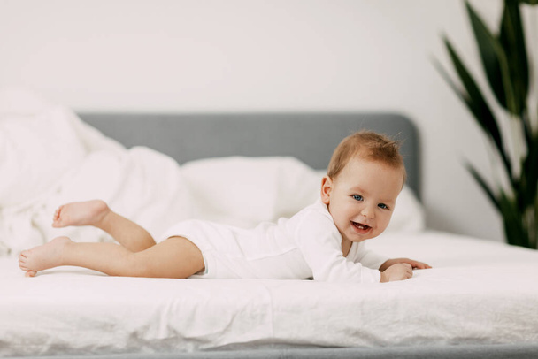 El recién nacido se encuentra en una cama blanca como la nieve debajo de las sábanas, se ríe y se complace - Foto, imagen