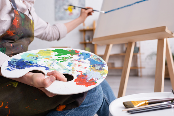vista recortada de la mujer madura sosteniendo paleta y pincel y pintura sobre lienzo - Foto, Imagen