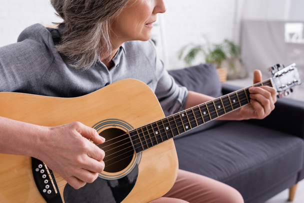 καλλιεργημένη άποψη της μεσήλικας γυναίκας με γκρίζα μαλλιά που παίζει ακουστική κιθάρα  - Φωτογραφία, εικόνα