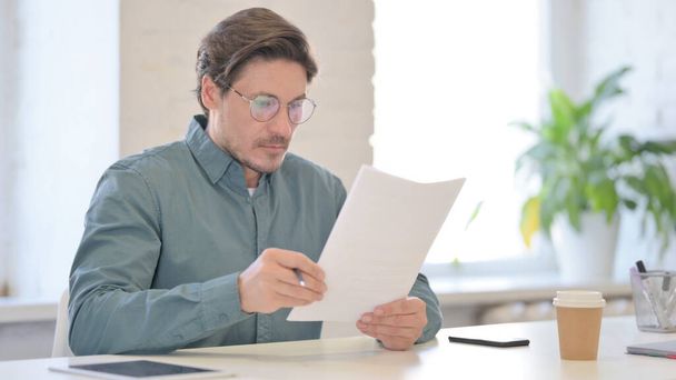 Middle Aged Man Reading Documents in Office - Foto, afbeelding