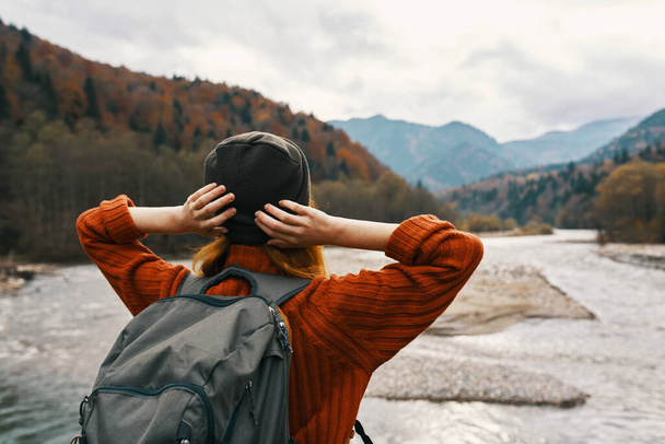 mujer viajera de vacaciones en las montañas en la naturaleza cerca del río toman de la mano detrás de su cabeza. Foto de alta calidad - Foto, imagen