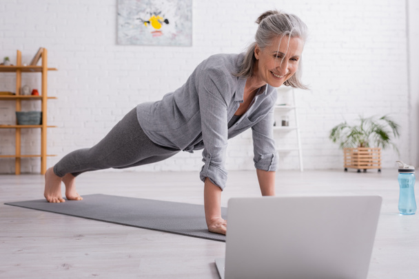 šťastný zralý žena cvičení a sledování jóga tutorial na rozmazaném notebooku  - Fotografie, Obrázek