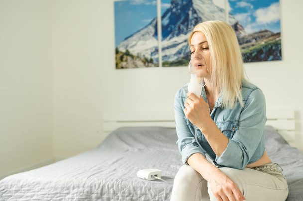 Πορτρέτο μιας νεαρής γυναίκας που εισπνέει στο σπίτι. Nebulizer αεροζόλ γυναίκα εισπνευστήρα φάρμακο μηχάνημα στο σπίτι. Ιός και γρίπη. - Φωτογραφία, εικόνα