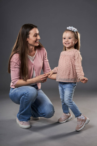 Young mother with her preschool little daughter on gray background - Foto, afbeelding