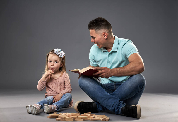Papa liest seiner kleinen Tochter ein Buch vor, während Spielzeugwürfel aus Holz herumliegen - Foto, Bild