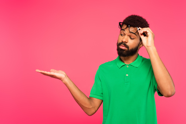 afrikanisch-amerikanischer Mann richtet Brille ein und zeigt mit der Hand isoliert auf rosa - Foto, Bild