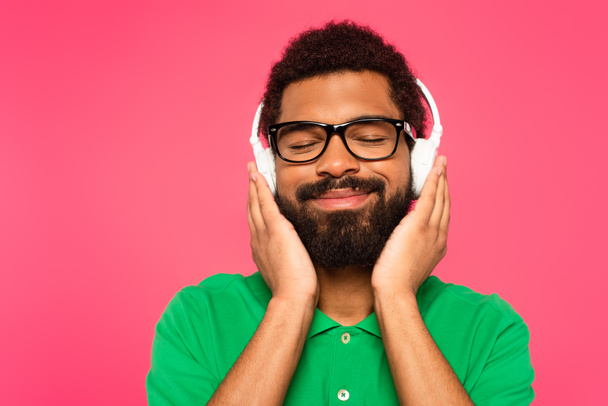 zadowolony african amerykański człowiek w okularach i słuchawki bezprzewodowe izolowane na różowy - Zdjęcie, obraz