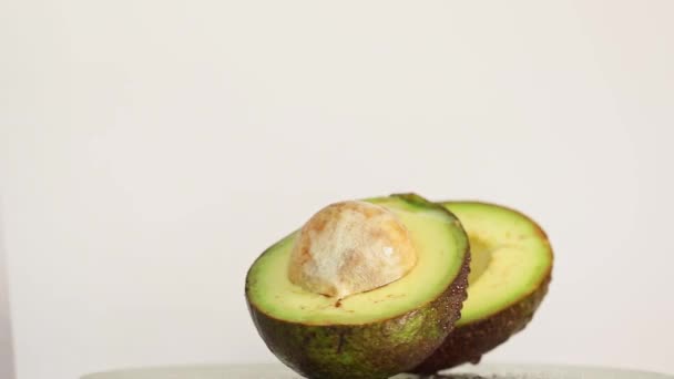Разрезать на два куска авокадо с каплями воды вращается на столе - Кадры, видео