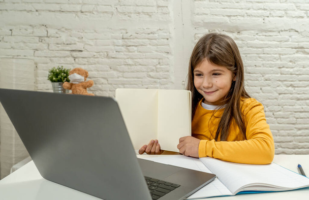 Happy Schoolgirl σε φορητό υπολογιστή που σπουδάζει online σε μια εικονική απομακρυσμένη τάξη στο διαδίκτυο στο σπίτι, καθώς τα σχολεία παραμένουν κλειστά λόγω του τελευταίου αποκλεισμού του κορωναϊού. COVID-19, εκπαίδευση, παιδιά και E- learning. - Φωτογραφία, εικόνα