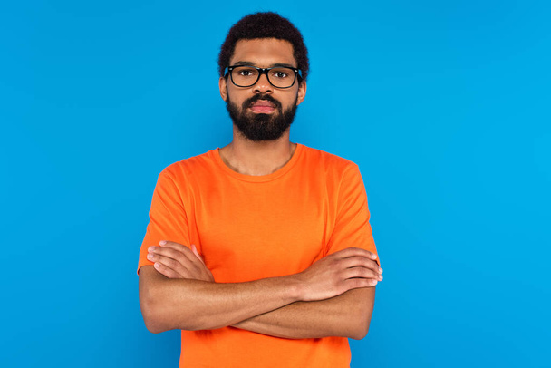 bearded african american man in glasses with crossed arms isolated on blue - Foto, Imagem