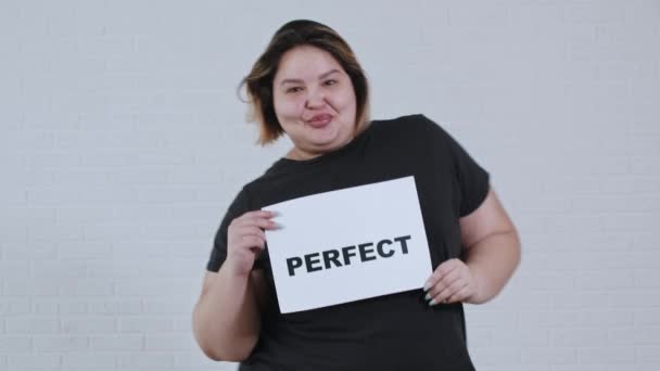 Concept lichaam positiviteit - een overgewicht lachende vrouw dansen en houdt een bord met de inscriptie PERFECT - Video