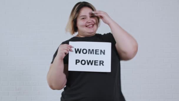 Αντίληψη θετικότητα του σώματος - μια υπέρβαρη χαμογελαστή γυναίκα χορεύει και κρατά ένα σημάδι με την επιγραφή WOMEN POWER - Πλάνα, βίντεο