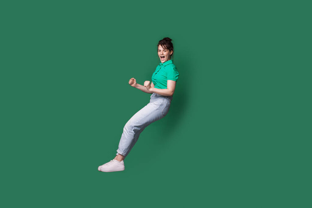 Fehér nő ugrál egy zöld stúdió falán sikoltozva, miközben reklámoz valamit. - Fotó, kép