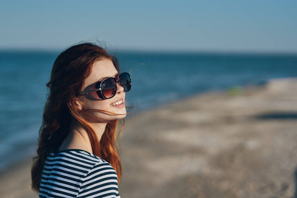 mujer en gafas y en una camiseta a rayas al atardecer o allí cerca de la vista al mar desde el balcón - Foto, imagen