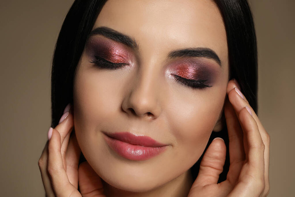 Beautiful young woman with evening makeup on brown background, closeup. Eye shadow product - Foto, Imagem