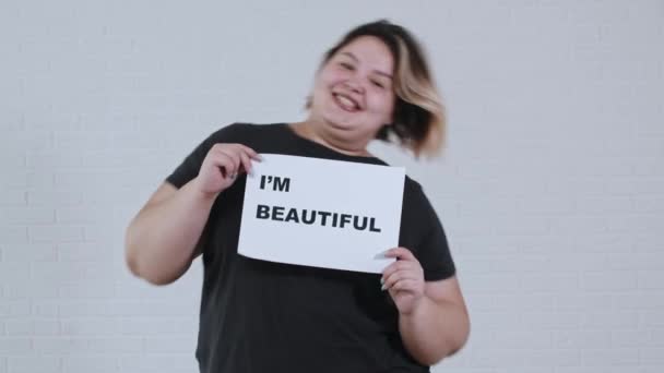 Koncept tělesné pozitivity - nadváha usměvavá žena tančí a drží znamení s nápisem IM BEAUTIFUL - Záběry, video