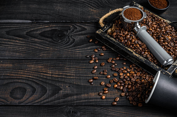 Gemahlener Kaffee in Portafilter für Espresso in einem Holztablett mit Kaffeebohnen. Schwarzer Holzhintergrund. Ansicht von oben. Kopierraum - Foto, Bild