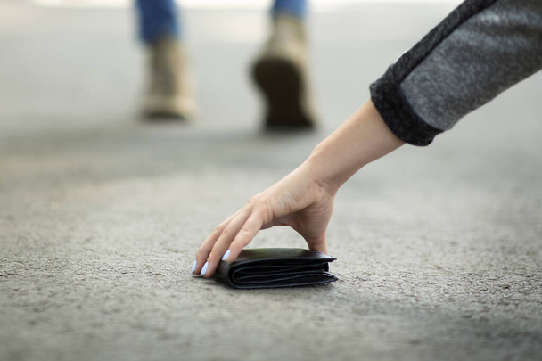 Vista da vicino della giovane donna che raccoglie il portafoglio perso sulla strada della città, spazio vuoto - Foto, immagini