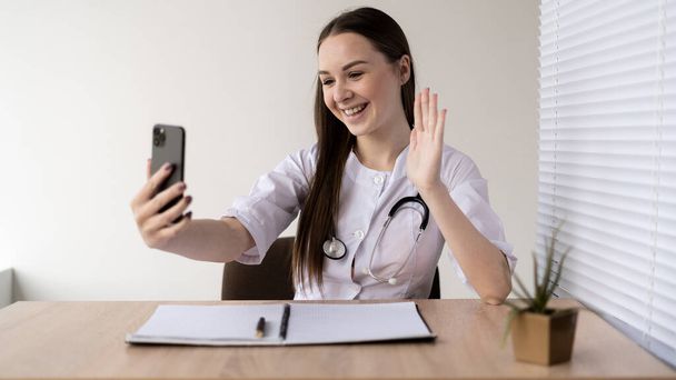 lady holds smartphone consultations on telemedicine, advises the patient in a virtual meeting, online and chat. Video call specialist help, headshot. - Фото, изображение