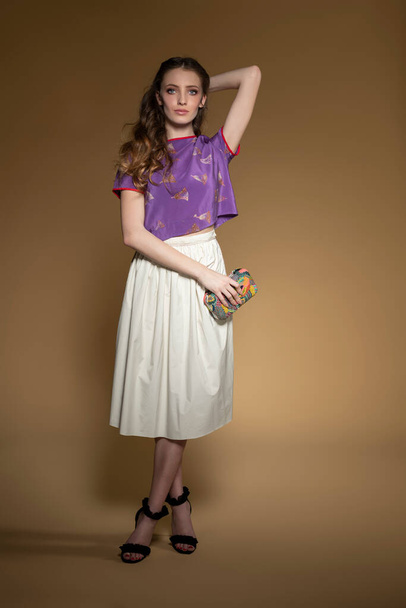 beautiful woman posinig on beige background , looking in camera , she is ready for a elegant summer night , dresssing. white gown and violet shirt. and black high heel shoes - 写真・画像