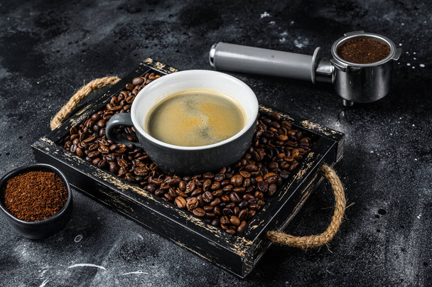 Kaffeetasse und Bohnen in altem Holztablett. Schwarzer Hintergrund. Ansicht von oben - Foto, Bild