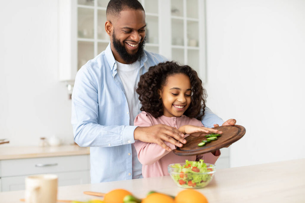 Cheerful afro father and daughter cooking salad together - Photo, Image