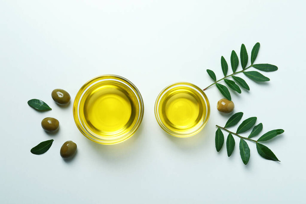 Schalen mit Öl, Oliven und Zweigen auf weißem Hintergrund - Foto, Bild
