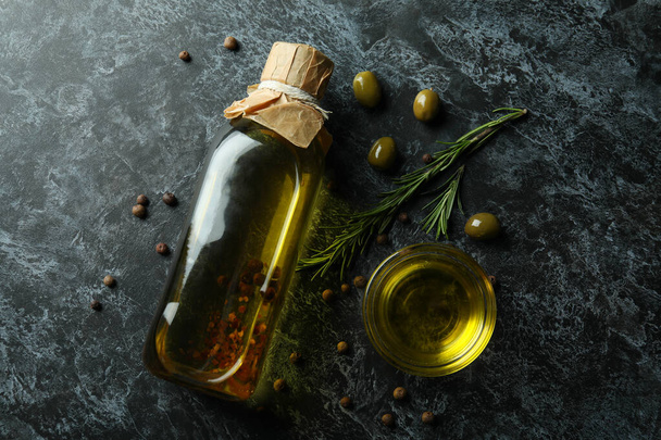 Botella y tazón con aceite de oliva y especias sobre fondo ahumado negro - Foto, Imagen