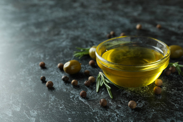 Bowl of olive oil, olives, pepper and rosemary on black smokey background - Фото, зображення