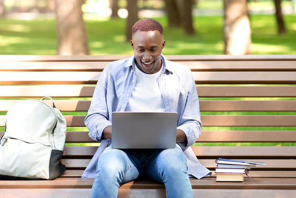 Aufgeregter schwarzer Student blickt auf Laptop-Bildschirm und kann seinen Erfolg im Park nicht fassen - Foto, Bild