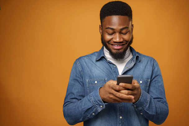 Portrait of young african american man using his smartphone against yellow background - Zdjęcie, obraz