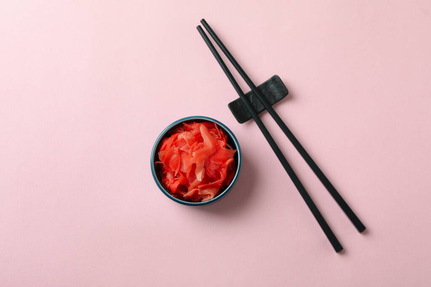 Чаша с красным маринованным имбирем и палочками для еды на розовом фоне - Фото, изображение