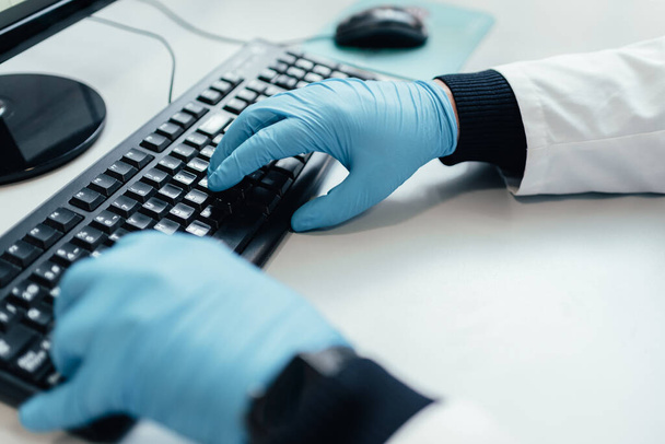 arts met handschoenen met behulp van een desktop computer. persoon die een rapport schrijft met de pc. typen op een toetsenbord. - Foto, afbeelding