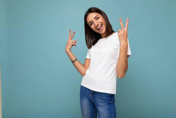 Fotografie pozitivní happu legrační mladé fascinující hezká brunetka žena s upřímnými emocemi na sobě ležérní bílé tričko pro mockup izolované přes modré pozadí s kopírovacím prostorem - Fotografie, Obrázek