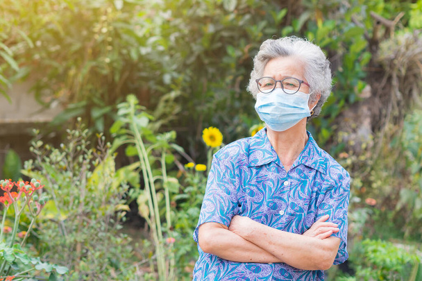 Portrait d'une femme âgée portant un masque facial et regardant la caméra debout dans un jardin. Masque pour protéger le virus, le coronavirus, les grains de pollen. Concept de personnes âgées et soins de santé. - Photo, image