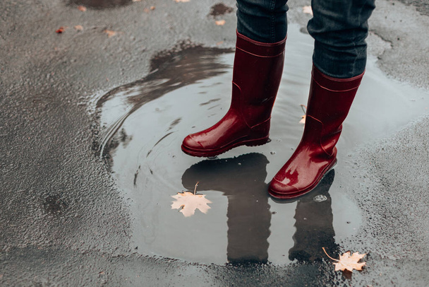 Samice stóp w czerwonych gumowych butach stoją w błotnistej kałuży pod deszczem jesienią - Zdjęcie, obraz