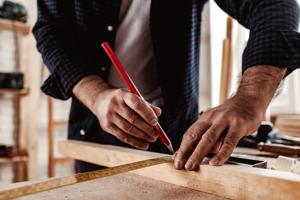 Carpenter makes pencil marks on a wood plank - Fotoğraf, Görsel