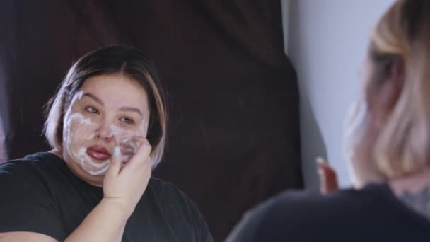 Une femme en surpoids applique le nettoyage de son visage devant un miroir - Séquence, vidéo