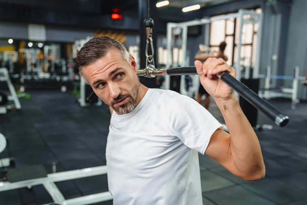 Attractive confident healthy sports man using seated lat pulldown machine in the gym - Fotografie, Obrázek
